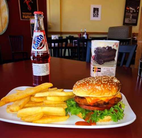 A plate with a sesame seed burger topped with lettuce and cheese, served with fries and a bottle of soda.