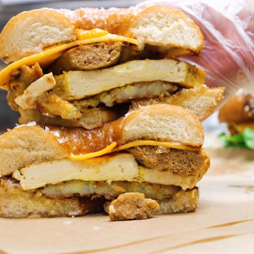 A stacked sandwich featuring layers of tofu, cheese, and a savory patty, all between two toasted buns.