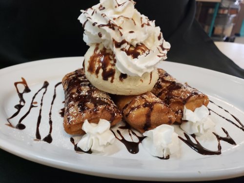 A plate of three fried desserts topped with a scoop of ice cream, whipped cream, and chocolate drizzle.
