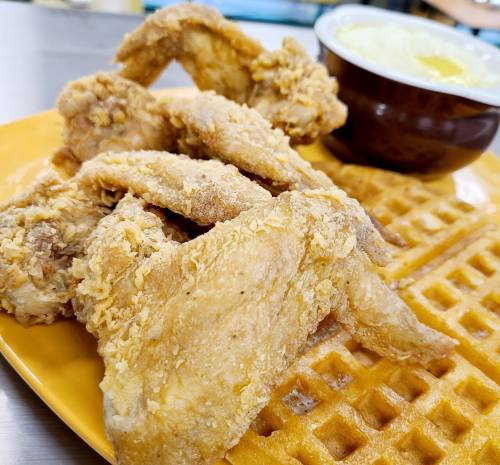 A plate of crispy fried chicken wings served with a side of waffles and a small bowl of syrup.