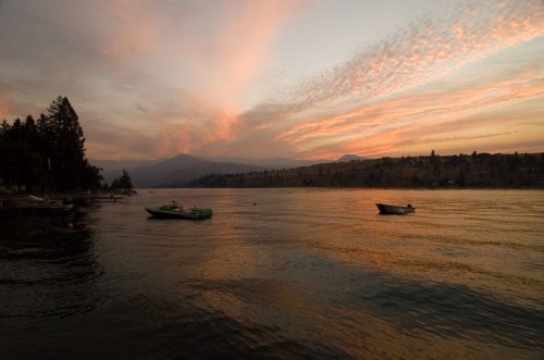 A serene lake at sunset, with boats floating and colorful clouds reflecting on the water.