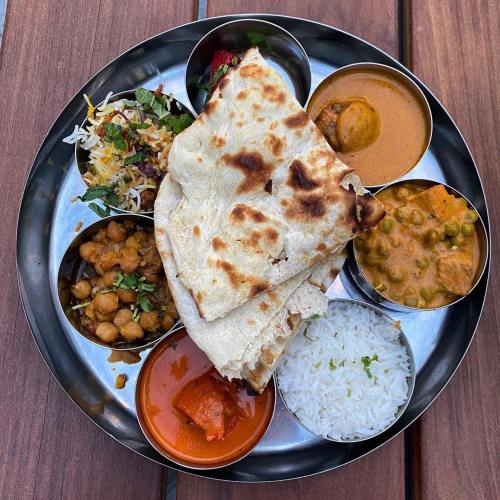 A traditional Indian thali featuring rice, bread, various curries, and a side salad, served on a metal platter.