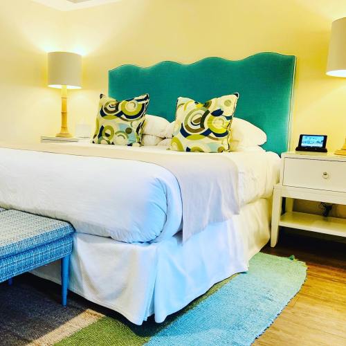 Cozy bedroom with a teal headboard, patterned pillows, bedside lamps, and a small seating area.