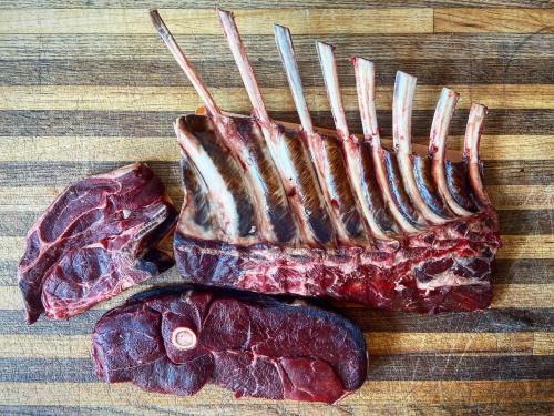 A raw rack of lamb with several chops, displayed on a wooden cutting board.
