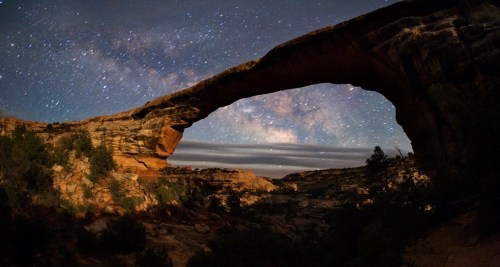 A stunning night sky filled with stars above a natural stone arch in a rugged landscape.
