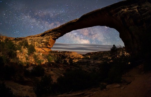 A stunning night sky filled with stars above a natural stone arch in a rugged landscape.