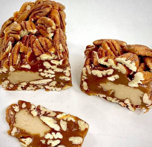 A close-up of a pecan caramel candy, with pieces cut to show the creamy center and nutty texture.