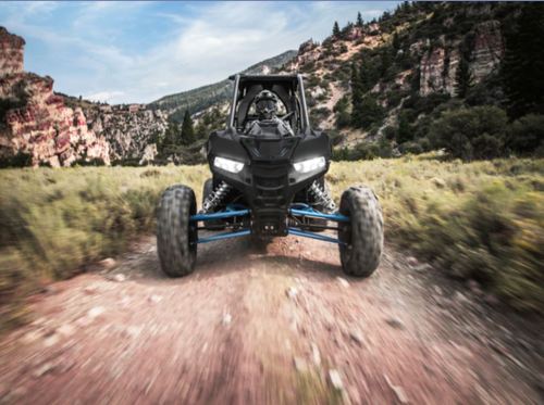 A black off-road vehicle driving on a dirt path surrounded by mountains and greenery.
