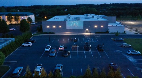 Aerial view of a parking lot at dusk, with cars parked and a building displaying a projection on its wall.