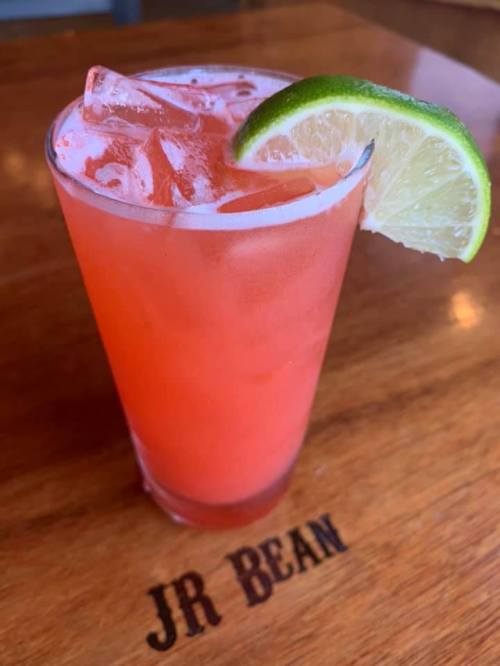 A refreshing pink drink with ice and a lime wedge, served in a clear glass on a wooden table.