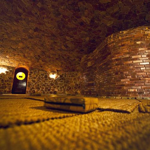A cozy, dimly lit room with stone walls and a textured floor, featuring a brick structure and a wooden door.