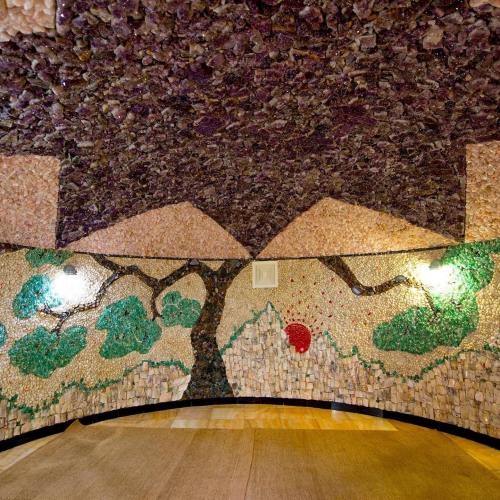 Interior view of a room with colorful stone mosaics depicting trees and a sun, featuring a textured ceiling.