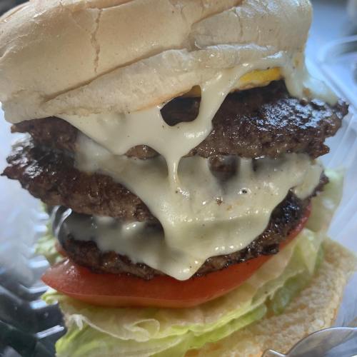 A towering burger with three beef patties, melted cheese, lettuce, and tomato, all in a soft bun.