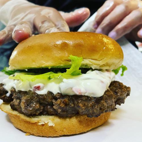 A close-up of a juicy hamburger with lettuce and mayonnaise on a toasted bun, with a hand in the background.