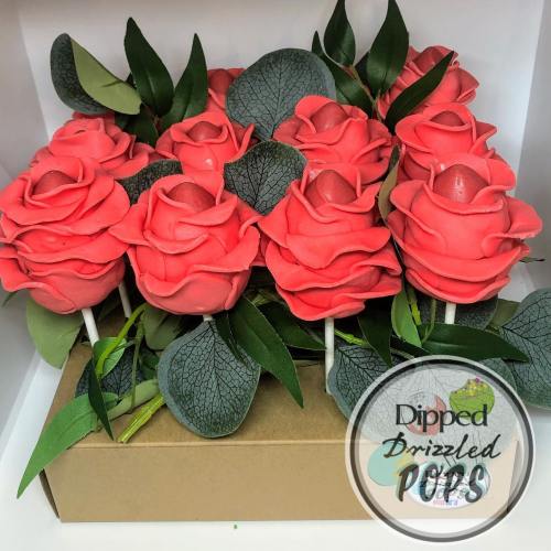 A bouquet of coral-colored rose cake pops with green leaves, arranged in a box.
