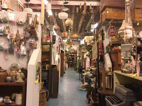 A narrow aisle in an antique shop filled with various vintage items, decor, and collectibles on both sides.