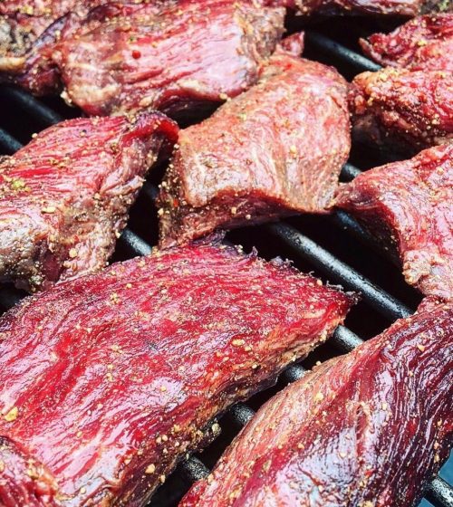 Close-up of marinated meat sizzling on a grill, showcasing a rich, red color and spices.