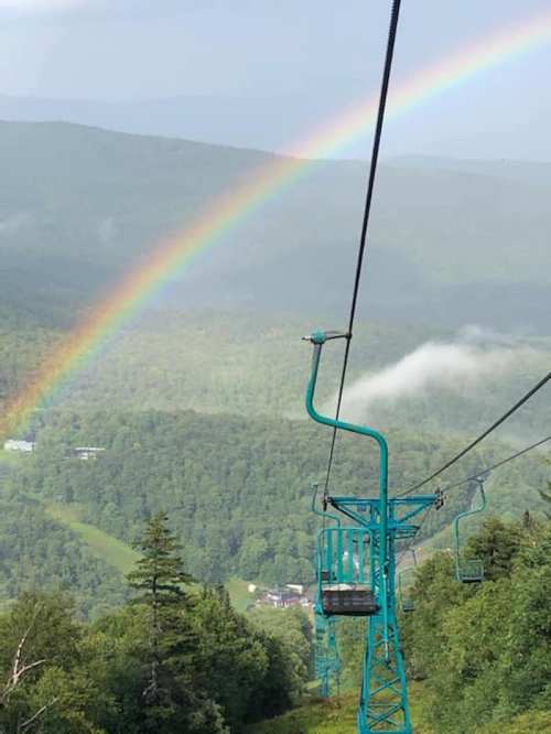 A ski lift chair against a backdrop of green mountains and a vibrant rainbow in the sky.