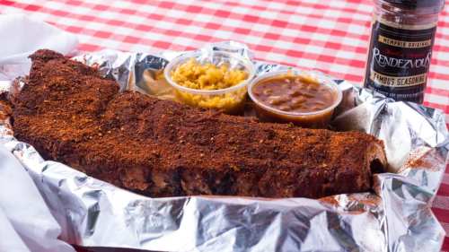 A platter of seasoned ribs with two sides: yellow rice and barbecue sauce, on a red-checkered tablecloth.