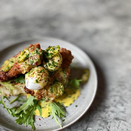 A plate of fried chicken topped with poached eggs, green tomatoes, and a drizzle of hollandaise sauce on arugula.
