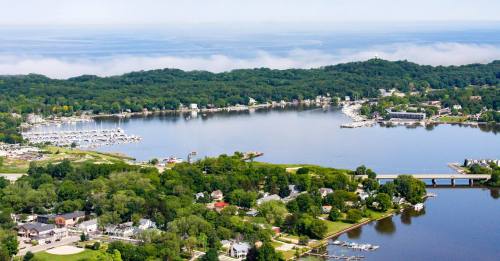 Aerial view of a serene lake surrounded by green trees, boats, and a small town along the shoreline.