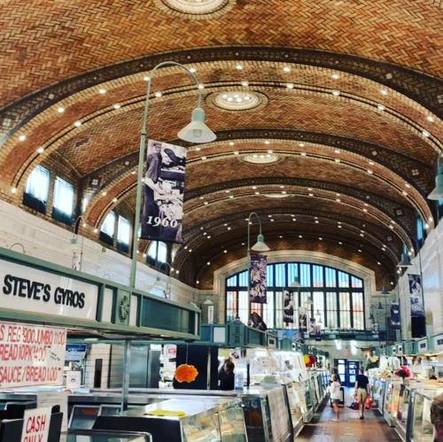 Interior of a market featuring a high, arched brick ceiling, bright lights, and vendor stalls with various goods.