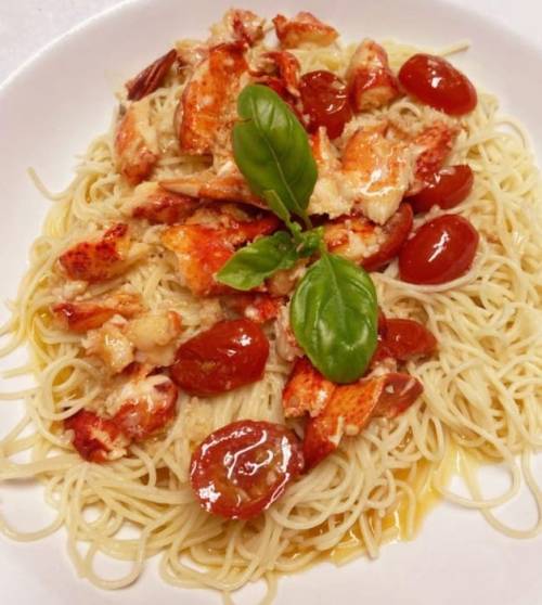A plate of spaghetti topped with lobster, cherry tomatoes, and fresh basil, drizzled with sauce.