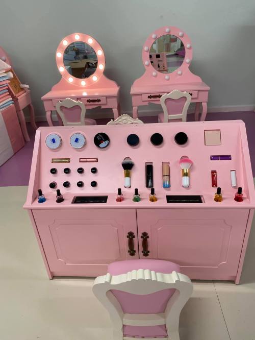 A pink vanity with various makeup products and tools, featuring mirrors and a chair in a bright, playful setting.