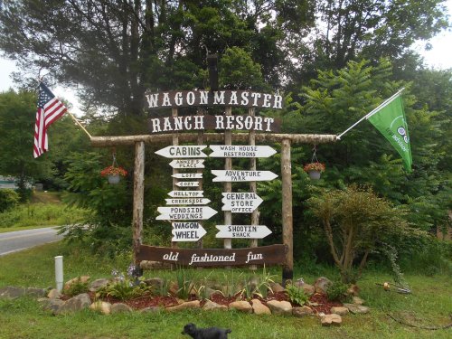 Sign for Wagonmaster Ranch Resort with directional arrows for various amenities, surrounded by greenery and flags.
