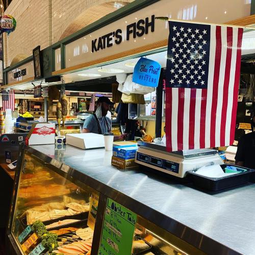 A seafood market stall named "Kate's Fish" with an American flag and various seafood displayed.
