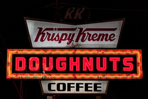 Krispy Kreme sign at night, featuring bright red "DOUGHNUTS" and "COFFEE" text with a retro design.