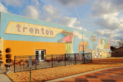 Colorful mural on a building wall featuring the word "Trenton" and various artistic elements against a blue sky.