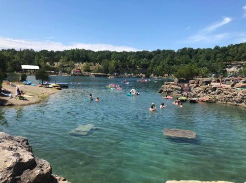 A sunny day at a swimming area with people enjoying the water, surrounded by trees and rocky shores.