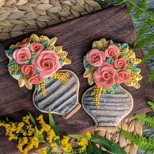 Two decorative cookie vases with colorful flowers, set against a natural background of leaves and woven texture.