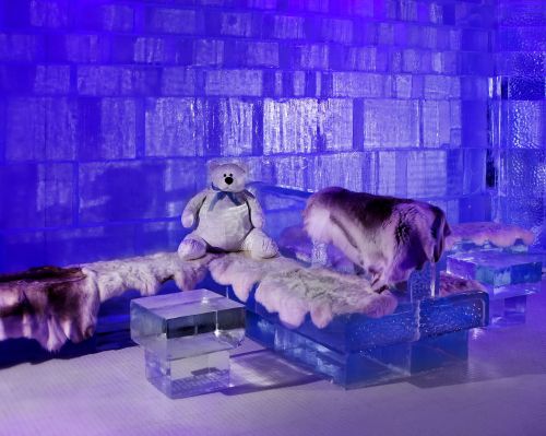 A cozy ice-themed room with a stuffed bear and fur-covered seating, illuminated by purple lighting.