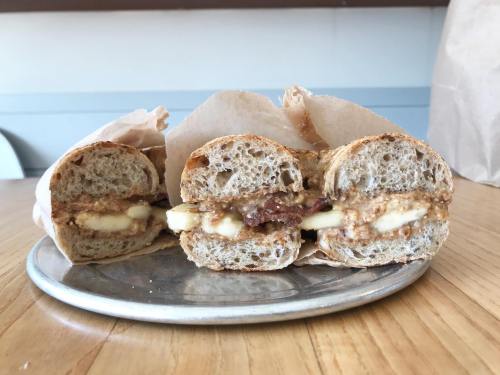 A plate with three halves of a sandwich made with whole grain bread, filled with apple slices and peanut butter.
