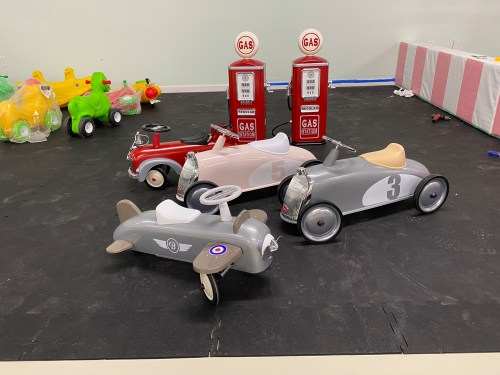 Three vintage-style toy cars in a play area, with two gas pump replicas in the background.
