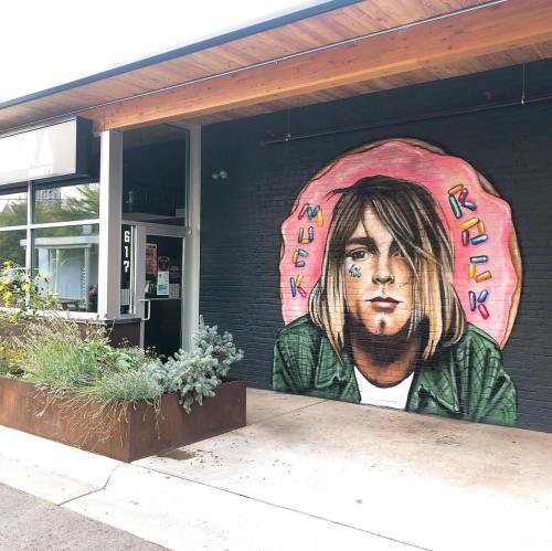 Mural of a person with long hair and a green jacket, surrounded by colorful text reading "Muck Rock."