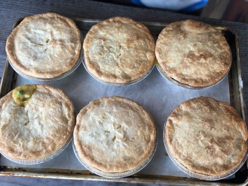 A tray of six golden-brown, freshly baked pot pies with flaky crusts.