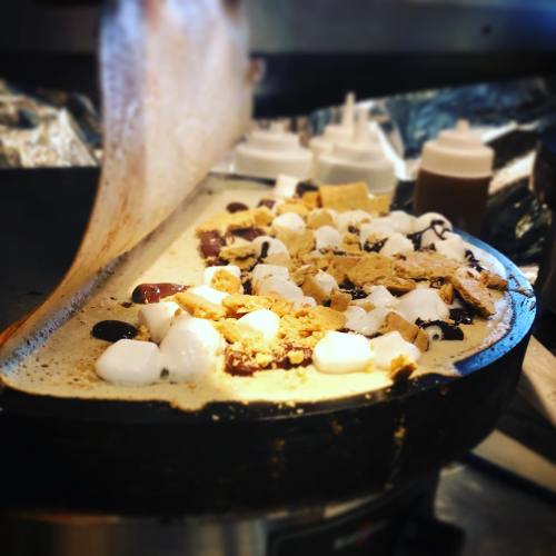 A crepe being prepared with chocolate, marshmallows, and graham cracker pieces on a hot griddle.