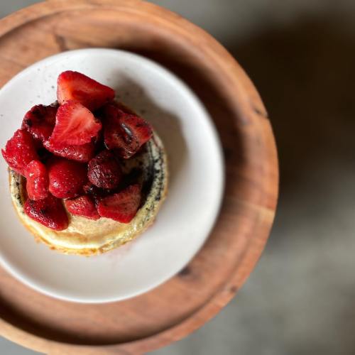 A round pastry topped with fresh strawberries and raspberries, served on a white plate atop a wooden tray.