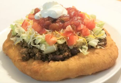 A delicious taco salad on a fried tortilla, topped with ground beef, lettuce, tomatoes, salsa, and sour cream.