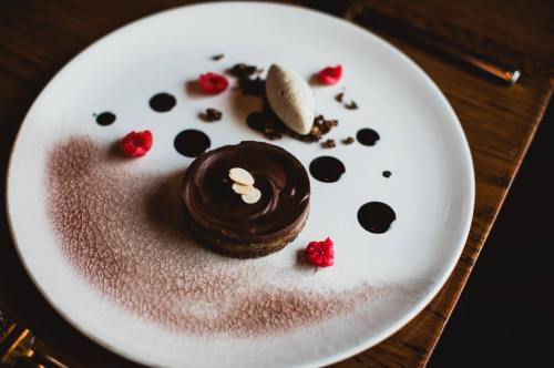 A chocolate dessert on a white plate, garnished with raspberry sauce, almond slices, and a scoop of ice cream.