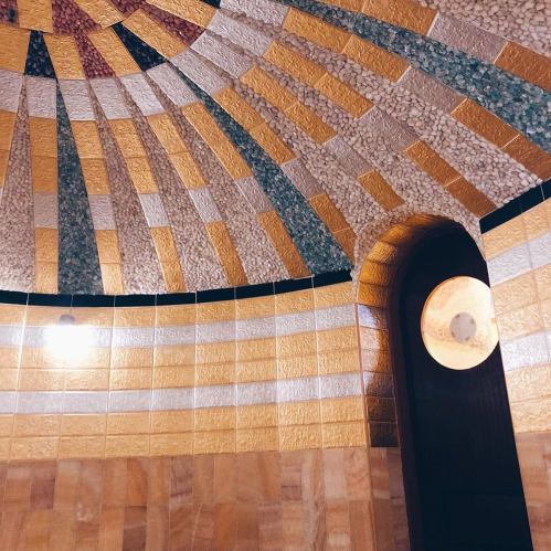 A close-up of a decorative ceiling with geometric patterns in gold, green, and white tiles, featuring a circular light fixture.