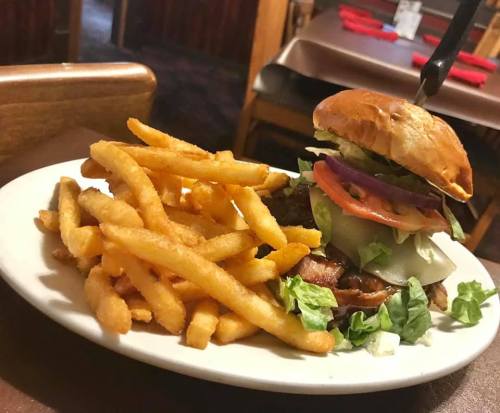 A plate with a stacked burger topped with lettuce, tomato, and onion, accompanied by a side of golden French fries.