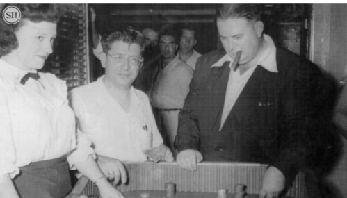 A black and white photo of three people playing a game, with two men and a woman in a vintage setting.