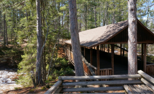 A wooden structure nestled among tall trees, overlooking a flowing river in a serene forest setting.
