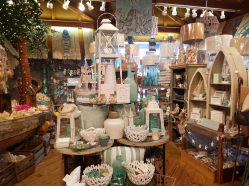 A cozy shop filled with coastal decor, including lanterns, shells, and decorative items in soft blue and white tones.