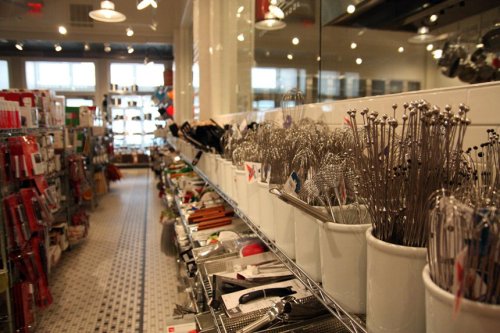 A kitchenware store aisle filled with various cooking utensils and tools displayed on shelves and in containers.