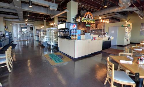 Interior of a casual restaurant featuring a service counter, drink station, and dining area with wooden chairs.